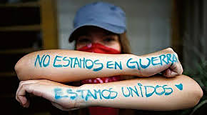Manifestante con consigna en los brazos cruzados: No estamos en guerra. Estamos unidos