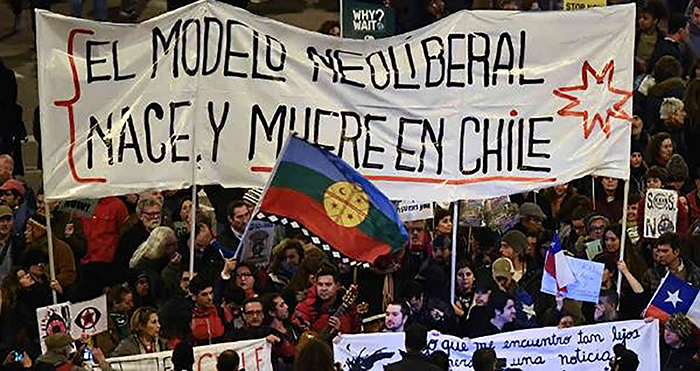 Manifestación con un lienzo que dice: El modelo neoliberal nace y muere en Chile.